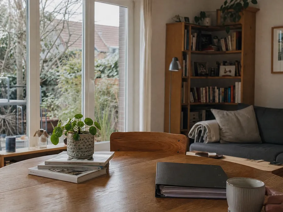 Ein bewohntes Wohnzimmer mit Holztisch und einer geschlossenen Dokumentenmappe am Tischrand, ruhige Alltagsatmosphäre