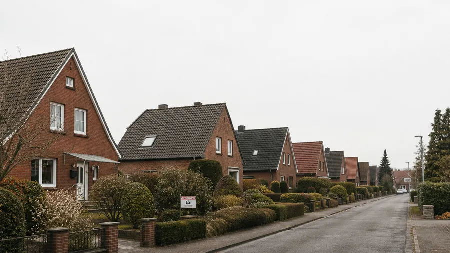 Ruhige norddeutsche Wohnstraße mit Klinker-Einfamilienhäusern und einem Verkaufsschild im Vorgarten.